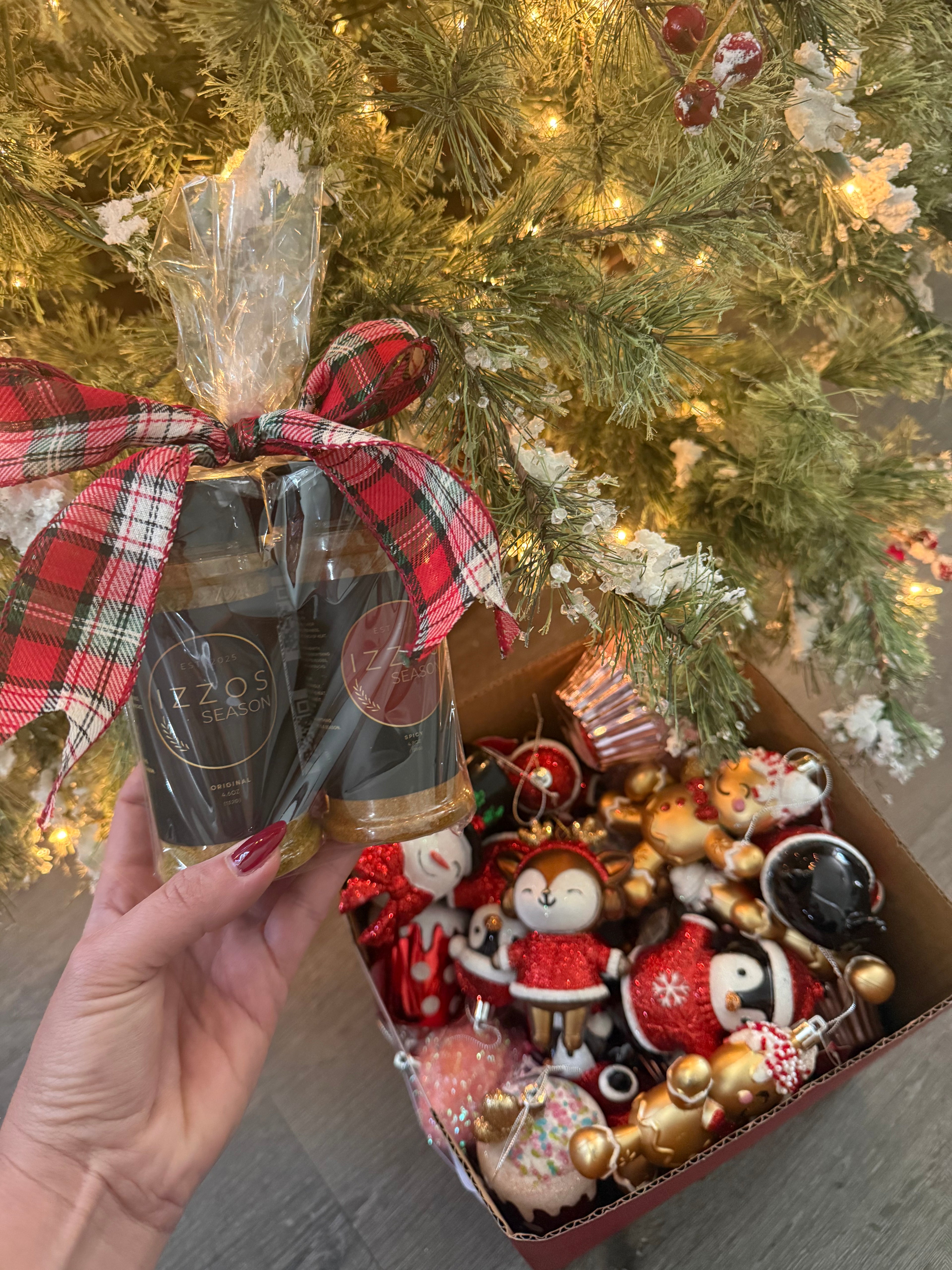 Izzo’s Season holiday seasoning gift set with plaid bow held in front of Christmas tree and ornaments.