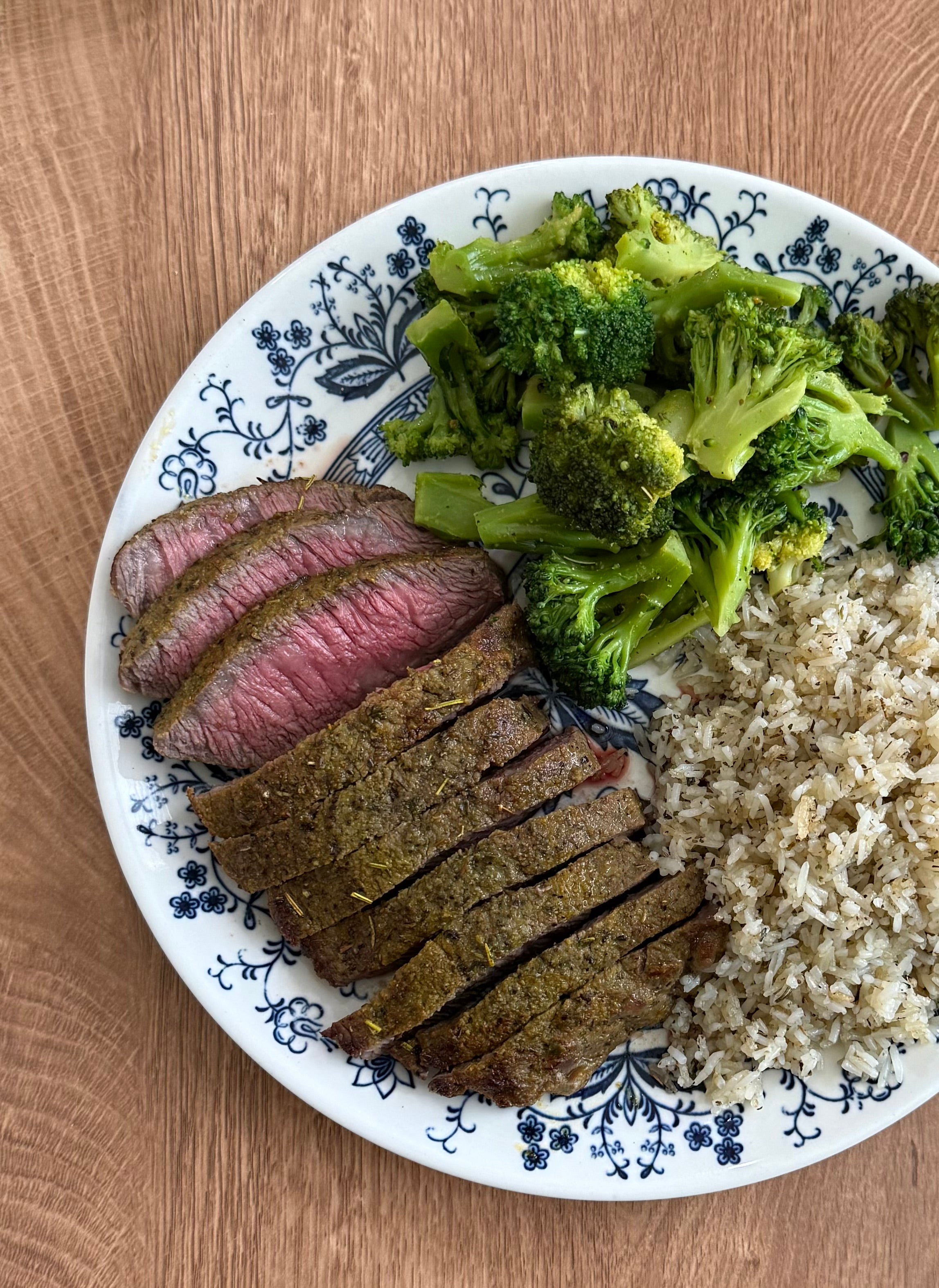 Plate with sliced steak, broccoli, and rice on a wooden table