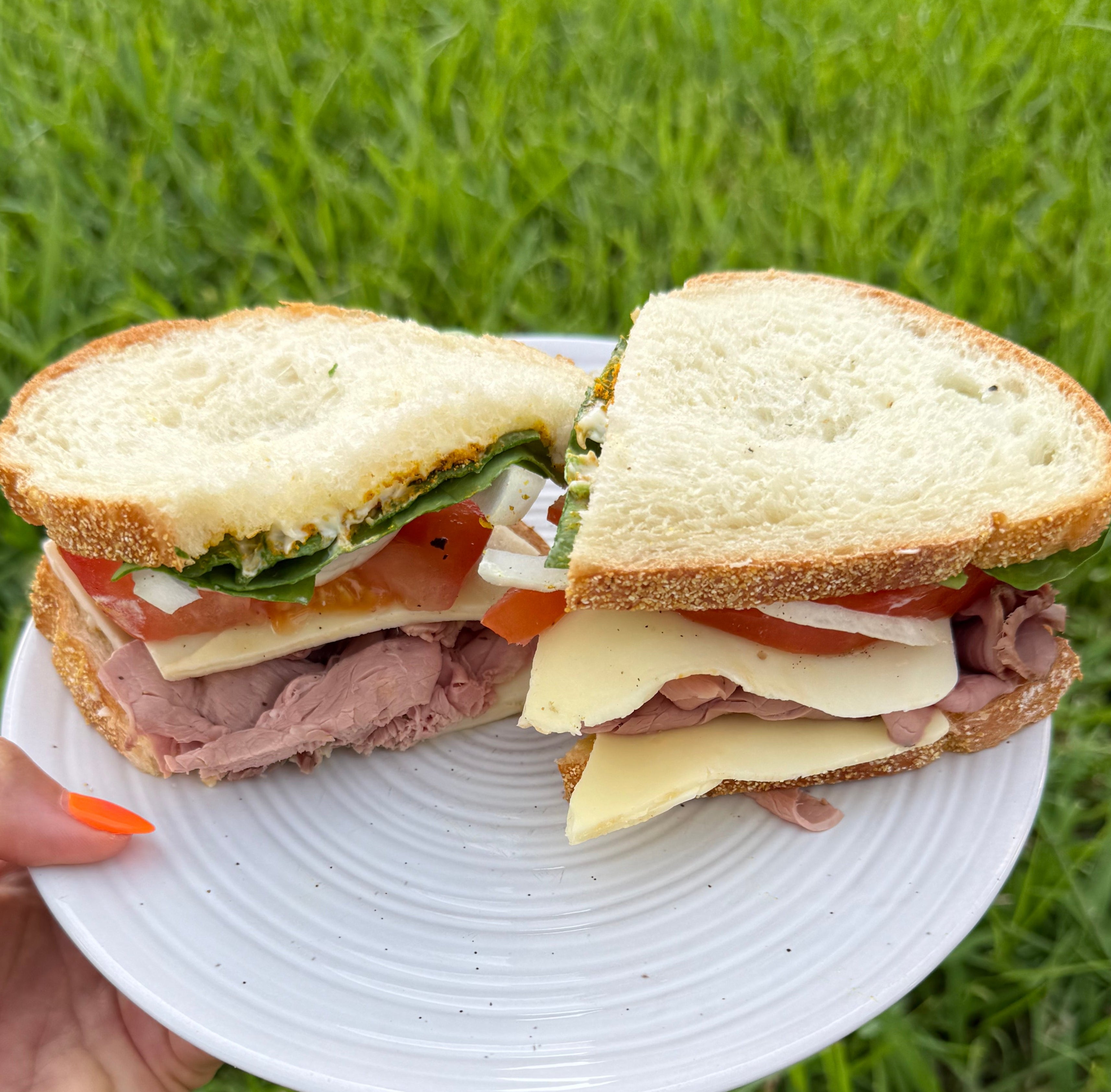 Half-eaten sandwich on a white plate held over grass