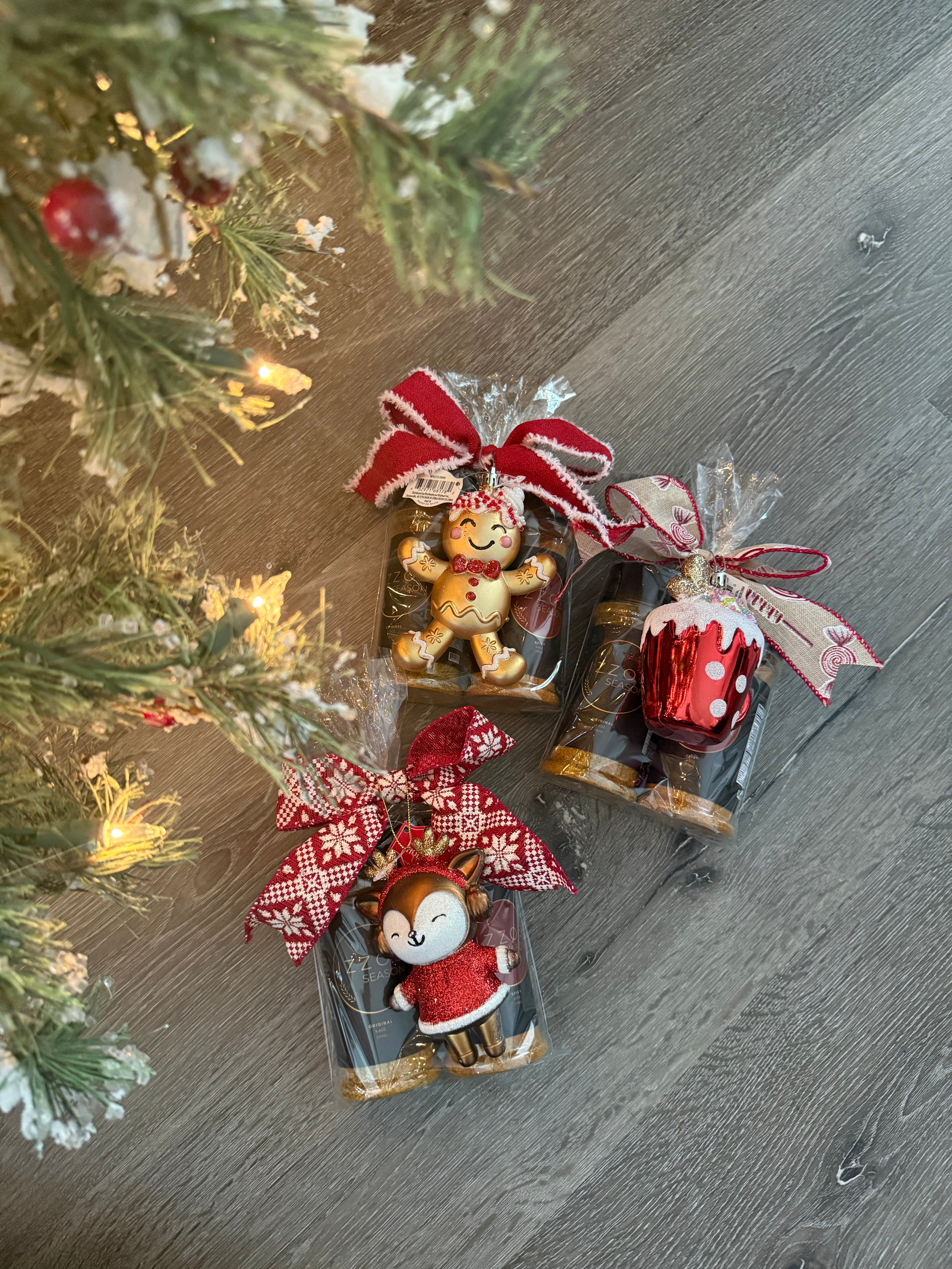 Izzo’s Season holiday gift bundle trio with gingerbread, reindeer, and cupcake ornaments under Christmas tree on wooden floor.